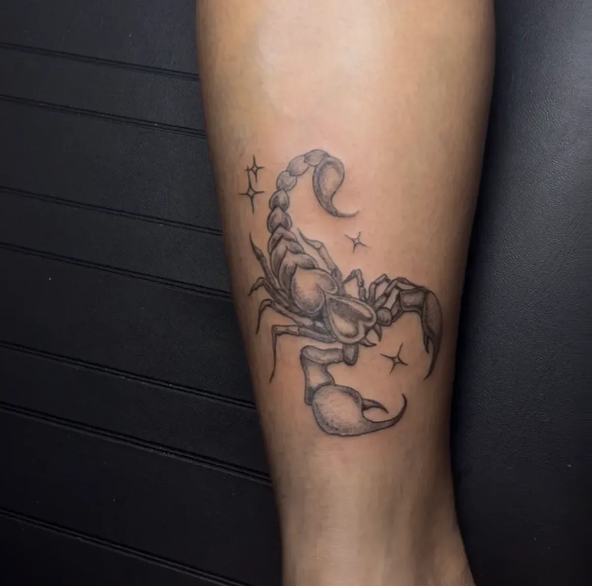 Tatuaje fine line de escorpión con estrellas y sombreado de puntos en la pierna