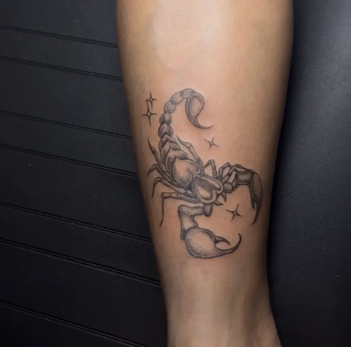 Tatuaje fine line de escorpión con estrellas y sombreado de puntos en la pierna