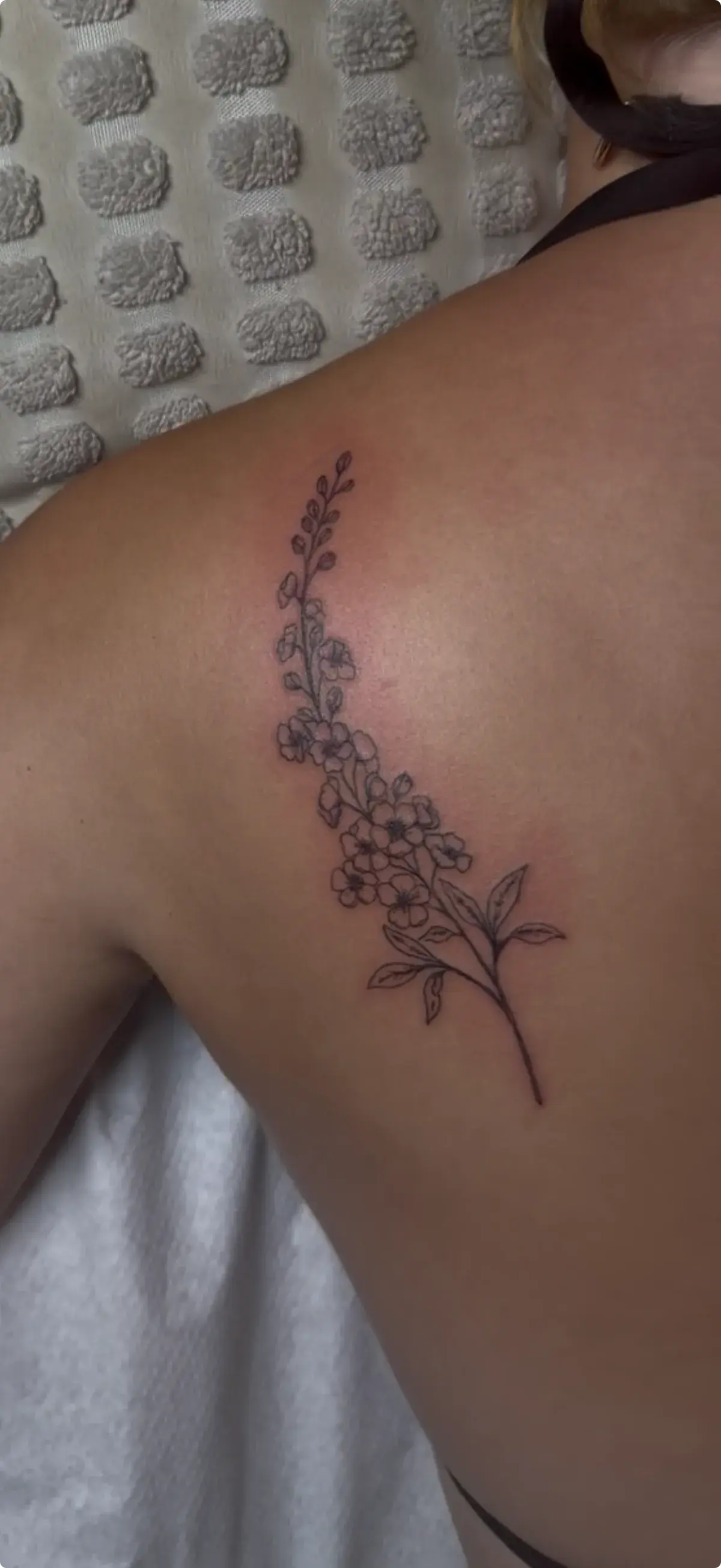 Tatuaje fine line de rama con flores en la espalda