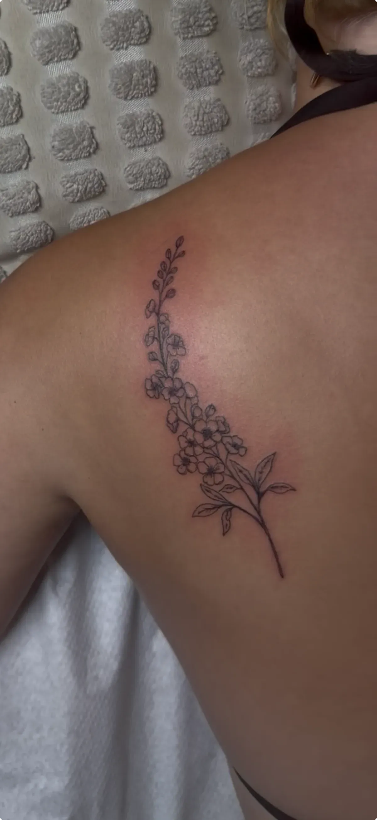 Tatuaje fine line de rama con flores en la espalda
