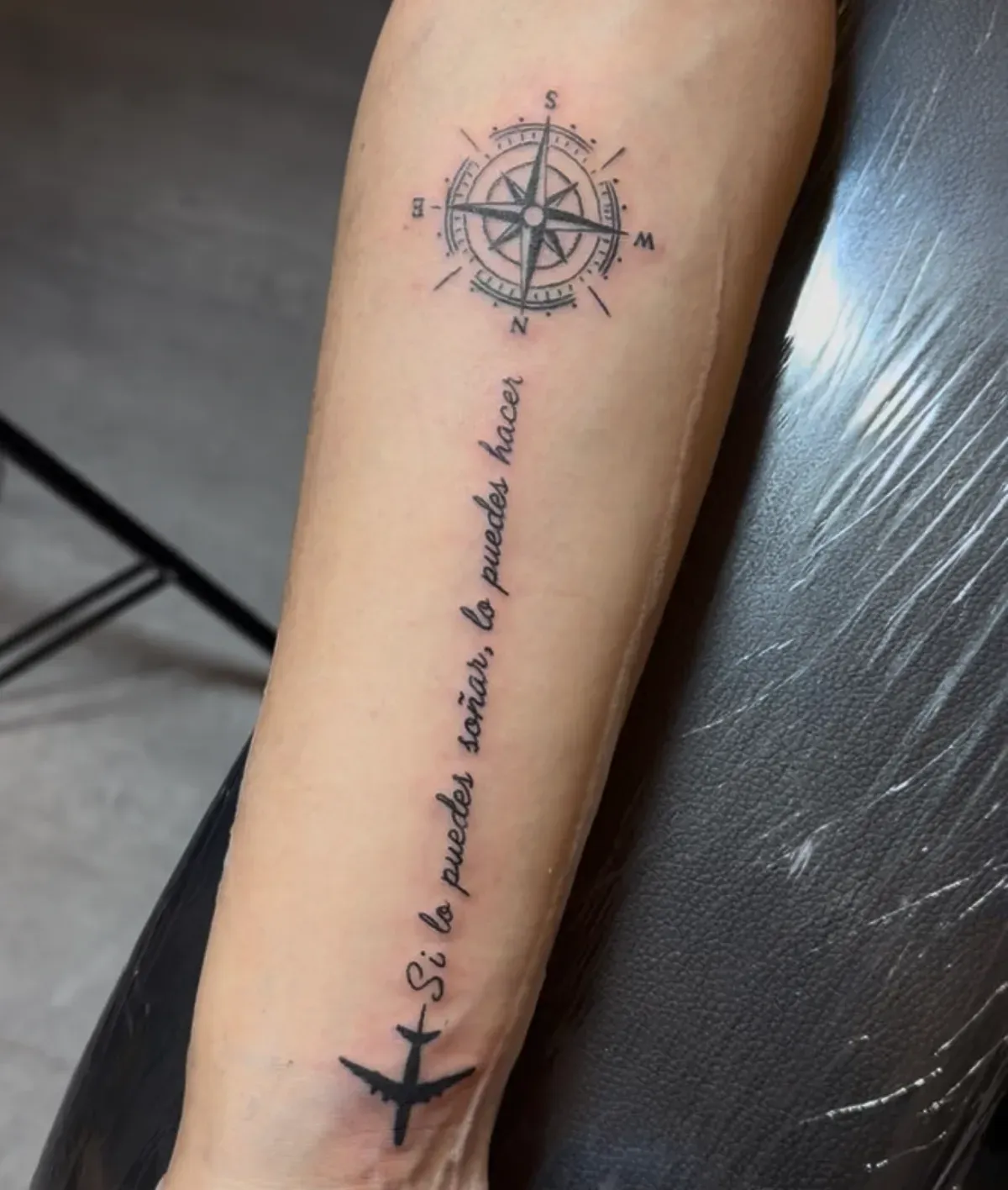 Tatuaje de brújula, frase «Si lo puedes soñar, lo puedes hacer» y avión en el antebrazo
