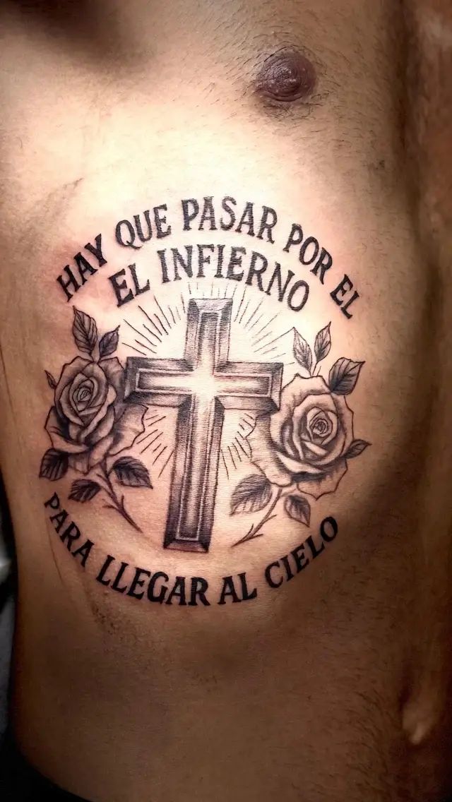 Tatuaje de frase con cruz y rosas en el pecho